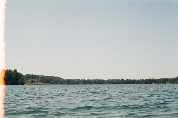 A picture of a very large lake surrounded by greenery. One side of the image has a white bar caused by light leakage.