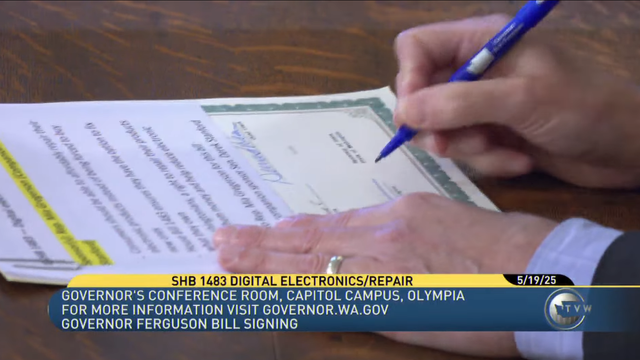 Still image of news broadcast from TVW showing a person signing a piece of legislation using a blue pen on a wooden table. The news overlay at the bottom of the screen has the headline "SHB 1483 DIGITAL ELECTRONICS/REPAIR 5/19/25" and the sublines:
"GOVERNOR'S CONFERENCE ROOM, CAPITOL CAMPUS, OLYMPIA
FOR MORE INFORMATION VISIT GOVERNOR.WA.GOV
GOVERNOR FERGUSON BILL SIGNING" with the TVW logo on the right.