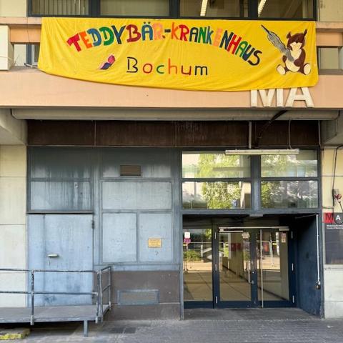 Eingang des Gebäudes der Medizinischen Fakultät der Ruhr-Universität Bochum mit einem bunten Banner mit der Aufschrift "Teddybär-Krabkenhaus Bochum".
