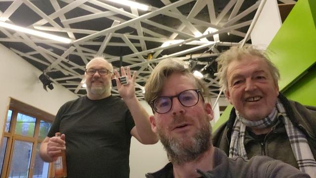 Die drei Mitglieder auf einem Selfie, das sie in offensichtlich ausgelassener Stimmung von sich machen, leicht von unten fotografiert.