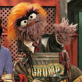 Purple fuzzy Muppet wearing a bad toupee, and a badly fitting suit, sat in a trash can.