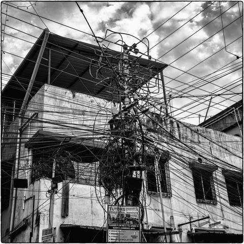 Quadratische Schwarzweissfotografie einer Telefonstange oder eines Strommastes mit unzähligen Drähten. 