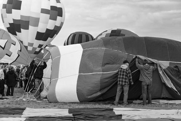 Black and white image of balloon crew members preparing a hot air balloon for launch at the 2018 Albuquerque Balloon Fiesta. The balloon is partially inflated, with people working along the seams. 