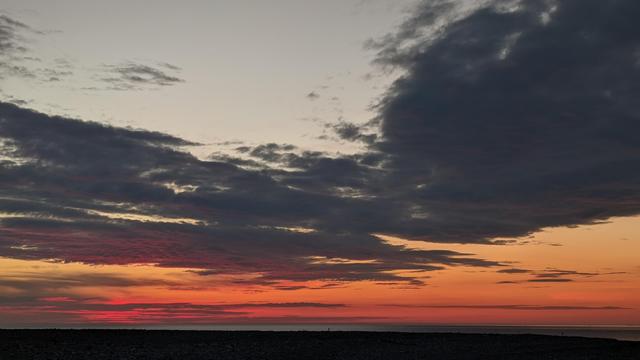 Historical Documentation in the form of a photograph of a rising sun over the ocean bay at Yirrell Beach in Winthrop, MA.  The sky is filled with vibrant colors of orange, pink, and purple, with the sun rising in the background. The clouds are scattered across the sky, creating a dramatic and moody atmosphere. The horizon line is visible in the distance, and the water is calm and still. The overall mood of the image is peaceful and serene.