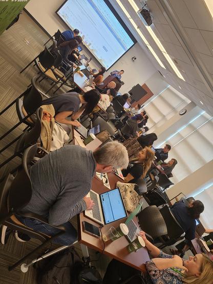 Room of workshop participants working on laptops in a conference during a presentation 