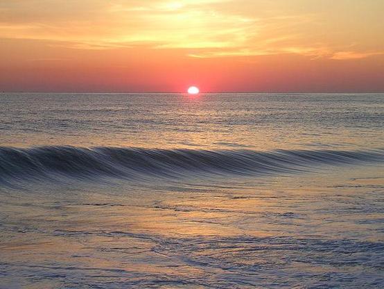 Creative commons
Photo d'un soleil levant au rond presque fuchsia mais petit, bien centré gauche-droite, mais la ligne d'horizon est sur le tiers supérieur, laissant la place à l'océan avec une vague grosse et douce qui fait une ligne au milieu.
Les nuages sont dorés, l'horizon orange, l'eau est gris-bleu et reflète les couleurs du ciel.