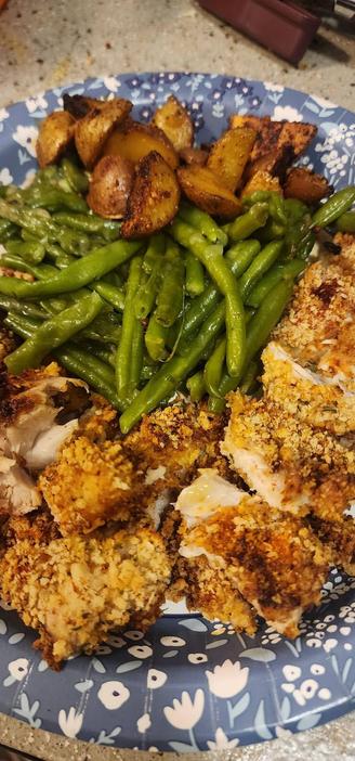 Picture of a paper plate with pan friend potatoes, green beans, and breaded chicken thigh