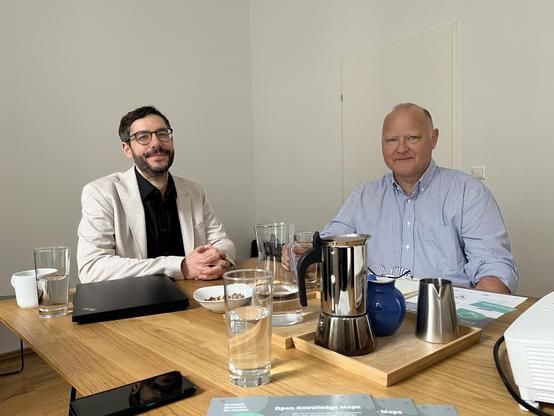 Peter Kraker (left) and Stefan Hanslik (right) seated at a meeting table in the Open Knowledge Maps office with coffee, water, and Open Knowledge Maps materials in front of them.
