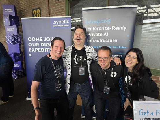 Four event attendees standing in front of amazee.io banners