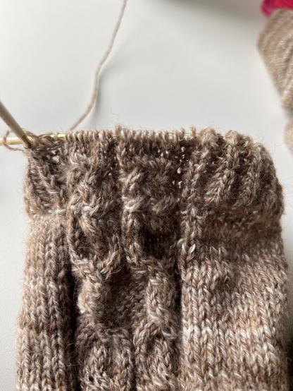 Knitted sleeve on small circular bamboo knitting needles. It has a panel with two small cables and stockinette stitch around it. About half of the cuff in brioche rib is done with the cable panel continued between the ribbed fabric.