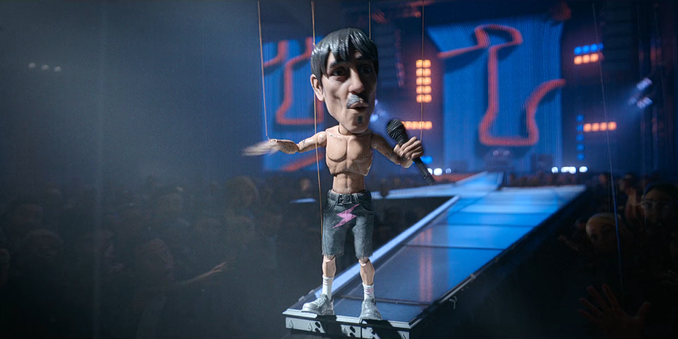 Cena do episódio Don't Stop da série Love, Death & Robots. Em destaque, uma marionete caricata de Anthony Kiedis, vocalista do Red Hot Chili Peppers. O boneco está sem camisa, vestindo bermuda jeans com um raio rosa e tênis, segurando um microfone e se apresentando em um palco iluminado. Ao fundo, há uma multidão animada e um grande telão com gráficos estilizados. A estética lembra um videoclipe animado com iluminação de show.