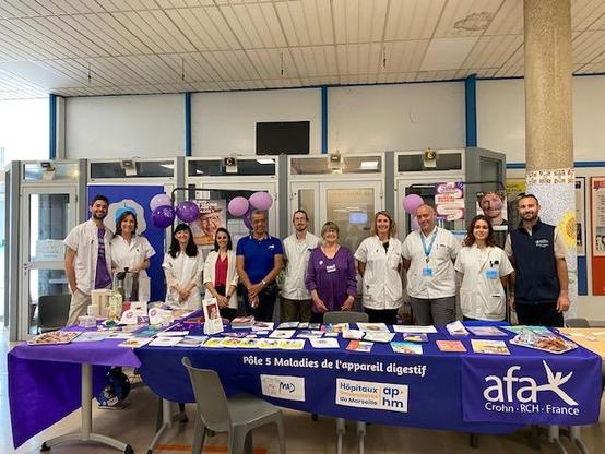 Photo de groupe de l’équipe hospitalière et des partenaires lors de la Journée MICI 2025 à l’Hôpital Nord, devant le stand d’information aux couleurs de l’AP-HM et de l’afa.