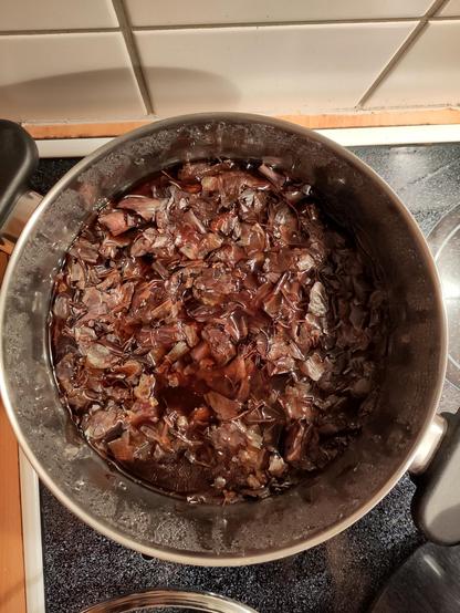 Onion skin broth in a pot for dyeing. It has a very intense brownish colour. The onion skins are floating on top of the broth.