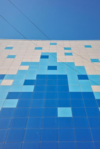 Wall of a multi-story building, taken from below. The whole wall is decorated with a pattern of square tiles of blue and white colors, which creates a pixel pattern.