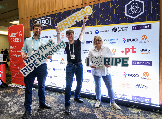 a photo of three people: two males on the left and a female on the right. they are holding printed hashtags that read: (from left to right) #myfirstRIPEmeeting, #RIPE90, I<3RIPE 