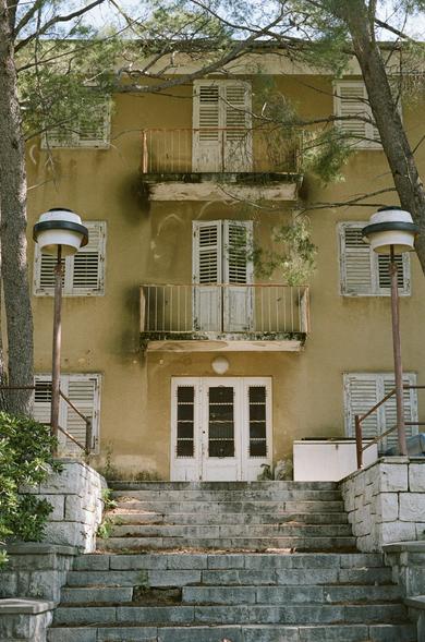 A weathered beige building with closed shutters and a big staircase leading up to it.