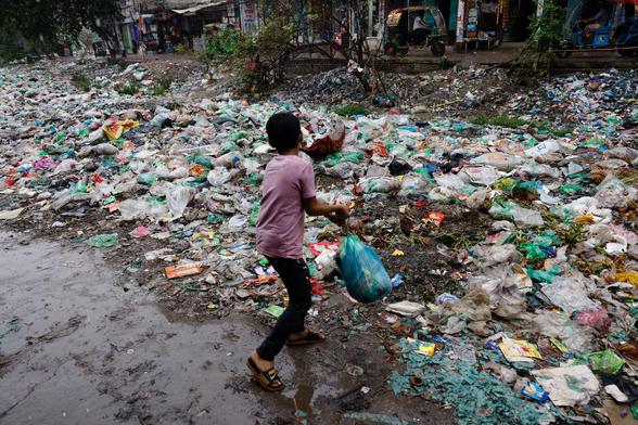 A boy throws a polythene bag full of waste into Shuvadda Canal which is under the pile of plastic waste, in Dhaka.