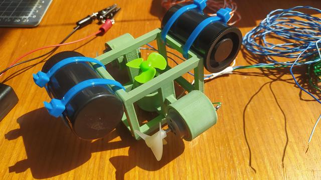 A small green frame with 3 motors and propellors and 2 35mm plastic film cans attached. 