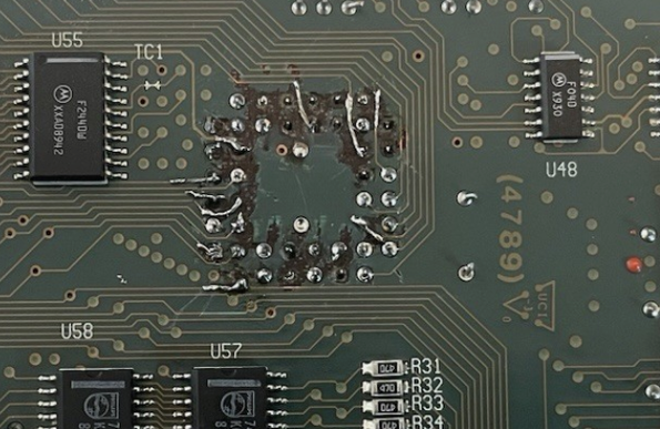 A close-up photograph of a circuit board, showing attempts to bridge over eroded or destroyed traces with solder and bodge wires.