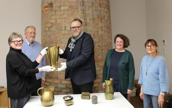 von links: Gabriele Bohnert, Erste Vorsitzende des Fördervereins Stadtmuseum Tonofenfabrik e.V., Heinrich Caroli, Zweiter Vorsitzender, Erster Bürgermeister Guido Schöneboom, Museumsleiterin Silke Höllmüller und Doris Hurst, Schriftführerin des Vereins. Gabriele Bohnert und EBM Guido Schöneboom halten mit weißen Handschuhen einen großen, glänzenden goldenen Krug in die Kamera.