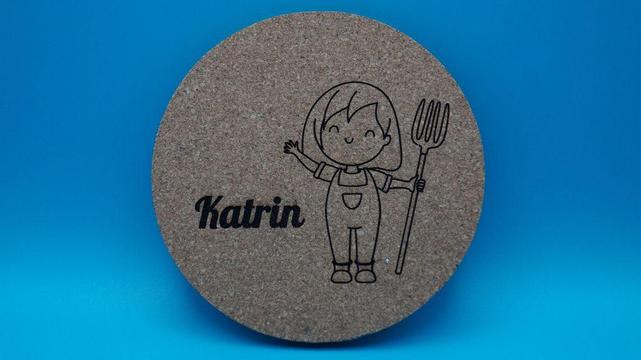 Runder Korkuntersetzer mit Bauernhofmotiv eines Mädchens in Latzhose mit Mistgabel und dem Namen „Katrin“.