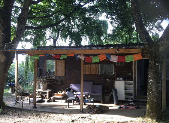 in a forest setting framed between two trees a cabin with a deck out front is draped under colourful Tibetan prayer flags