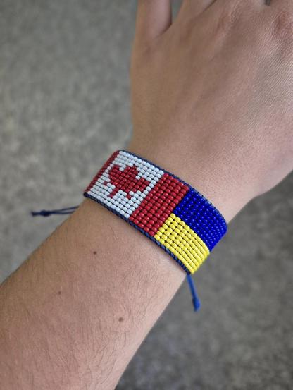 The photo shows a handmade beaded bracelet, half of the bracelet is the flag of Canada, the other half is the flag of Ukraine.