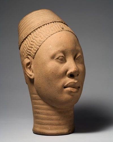 A terracotta sculpture of a human head, featuring highly naturalistic, detailed facial features and intricate hair styling. The piece has a smooth finish and is the reddish tan color of natural fired clay. It is the artwork of the Ife Empire (1000-1400 CE) depicting a person of high status. 