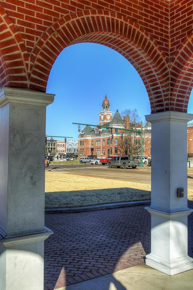 A picturesque view captures a historic courthouse framed by the arches of a brick pavilion
