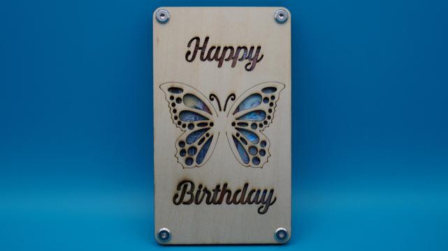 Holzrahmen mit gelasertem Schmetterling und „Happy Birthday“-Schriftzug, hinterlegt mit Geldschein, verschraubt als kreative Geschenkidee.