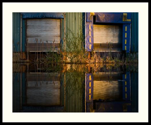 colour - Abandoned and slightly dilapidated, two bay loading ramp. The gently down sloping ramp has filled with water over time, now acting as a mirror. Reeds and other vegetation have started to grow against the building.

Shot during golden hour on a mostly cloudy morning. A gap in the cloud cover partially lit up this scene with nice warm light.