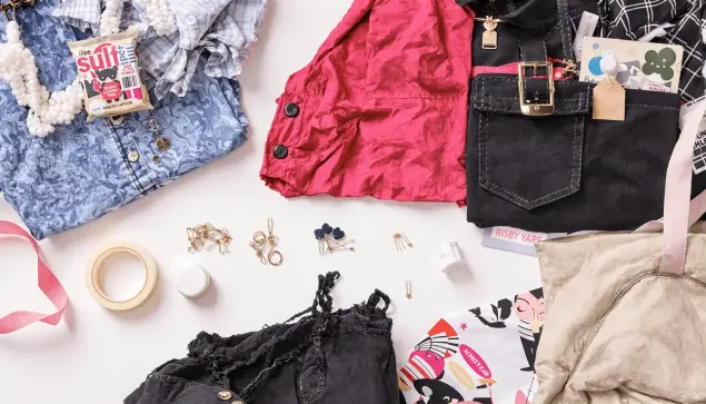 Flat lay of fashion essentials: double-sided tape, safety pins, sewing kit, and neatly arranged clothing on a clean surface.