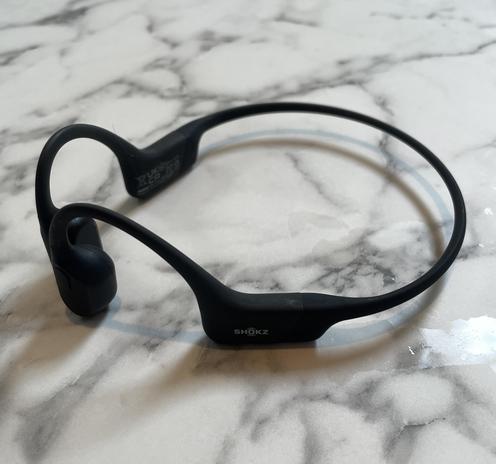 A pair of black Shokz headphones on a marble-esque counter.
