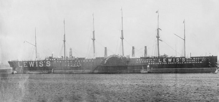 Black and white photograph of the Great Eastern ship, starboard side on, with giant white letters painted on the hull "LEWIS'S... are the friends of the people"... on the paddle wheel housing "the bon marche live" ... forward: "Ranelach St Liverpool, Lewis's, bon marche, basnett st, Manchester, Sheffield, Birmingham"