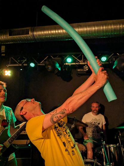photo de concert du groupes Les Remplaçants avec le chanteur brandissant une frite de piscine verte
