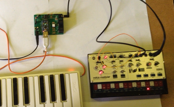 Photo of my custom USB MIDI to CV PCB previously mentioned, with a USB MIDI controller plugged in; and connected via the CV/GATE link to a Korg Volca Modular synth.
