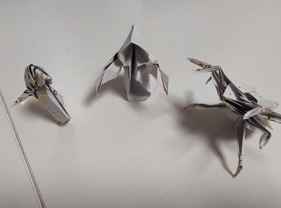 Three rough looking origami figurines, folded from Christmas themed wrapping paper. They are: a snake, a hooded cultist / ghost & a giant spider.