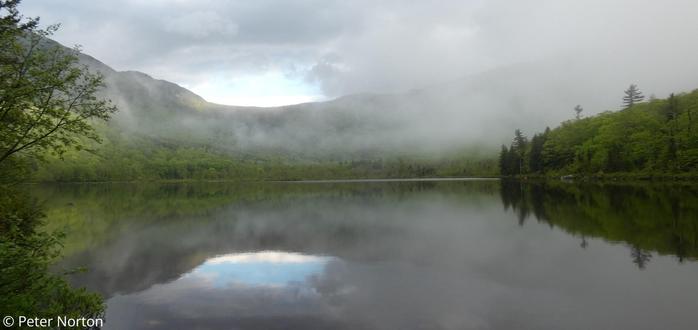 The mist is lifting from Basin Pond and there is a small opening in the clouds that reflects as blue sky in the surface of the pond.