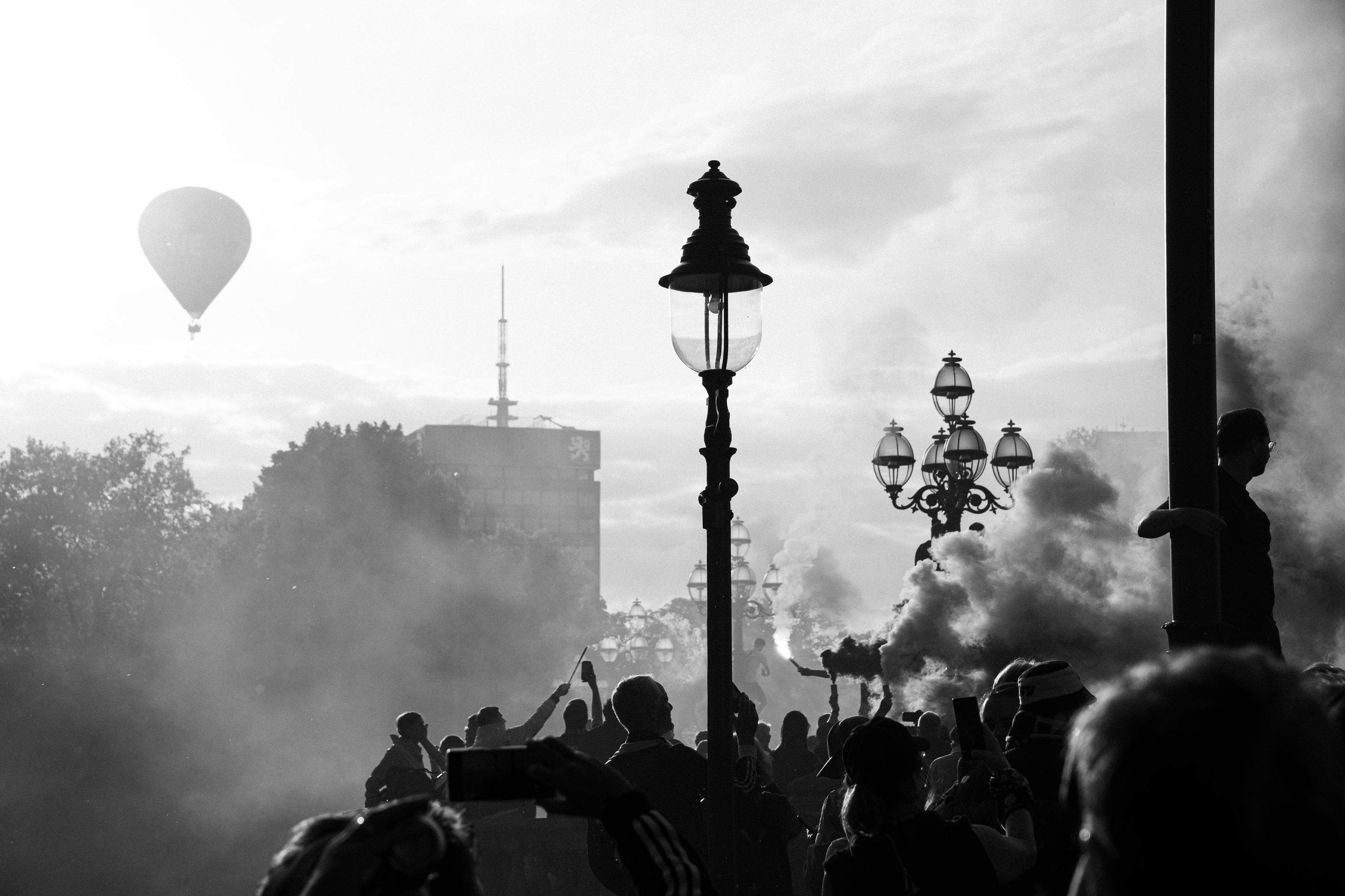 Photo of football fans burning pyrothechnics on a brige, with a hot air balloon in the background.