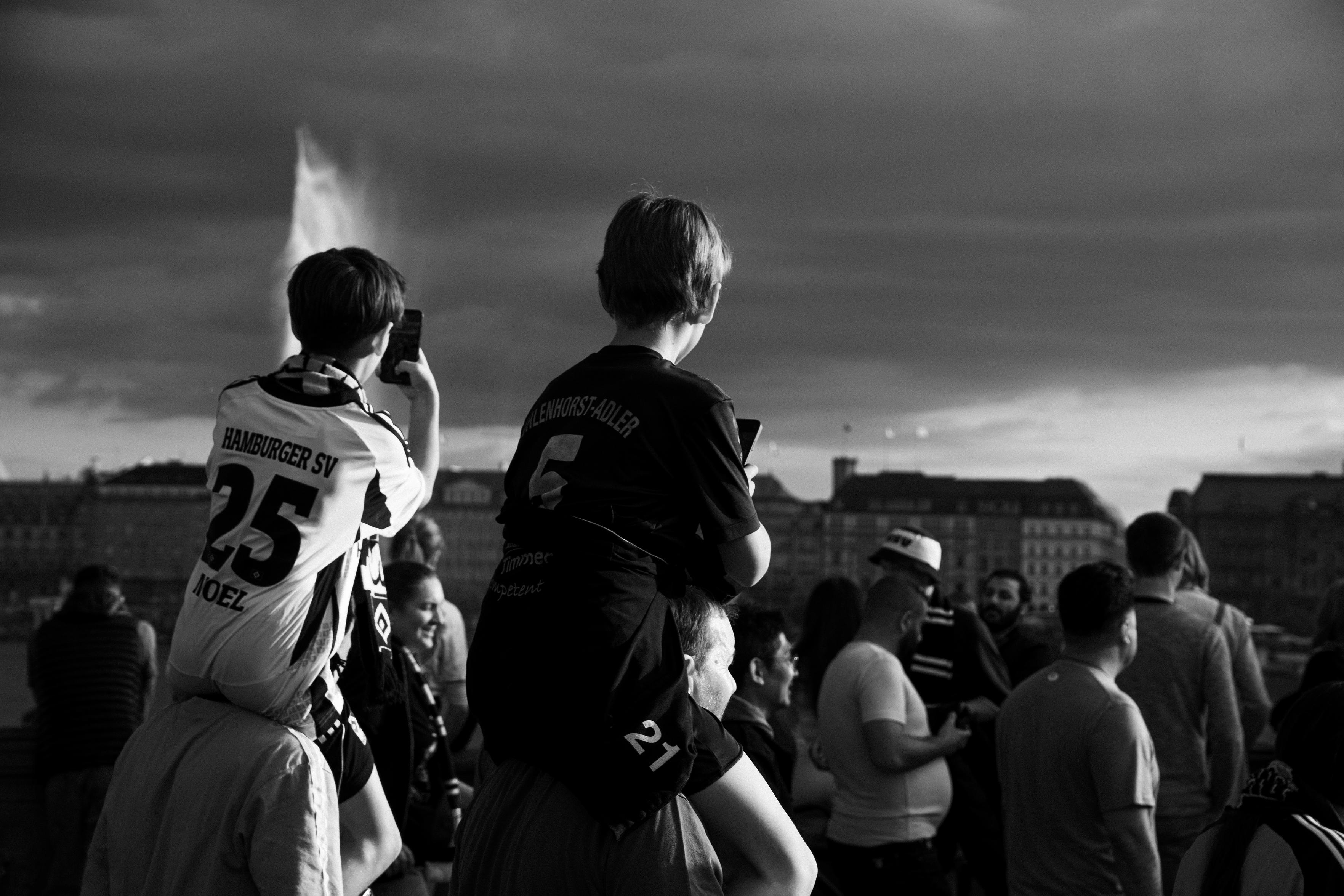 Photo of two kids in foorball uniforms sitting on the shoulders of adults and holding smartphones.