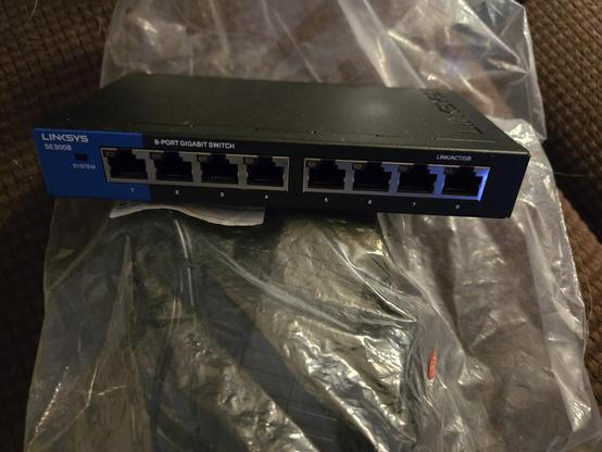 Picture of a Linksys 8-port gigabit switch with a clear back under it containing the power block for it.