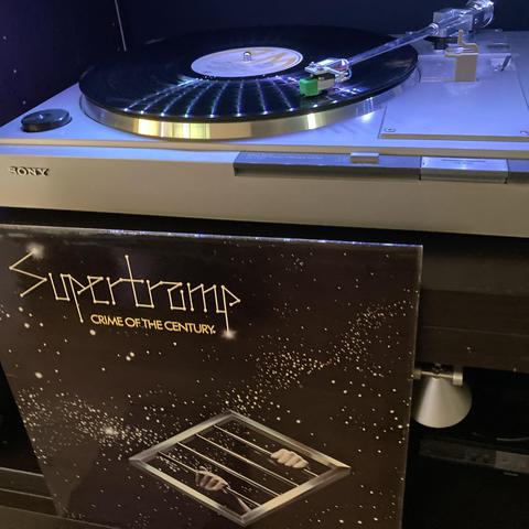 The album cover sits beneath a turntable playing the record. 