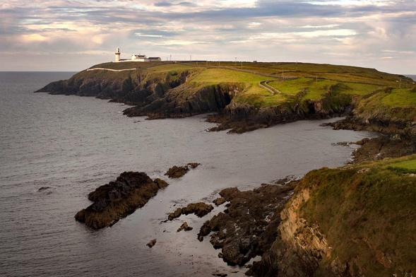 Une bande de terre s’avance dans l’océan depuis la droite. Au bout, un phare blanc réfléchit la lumière matinale. L’herbe rase est éclairée par le soleil levant, à certains endroits seulement. Le ciel est parcouru de nuages, mais il n’est pas menaçant. Sur la gauche, l’eau sombre contraste avec les éléments éclairés.  