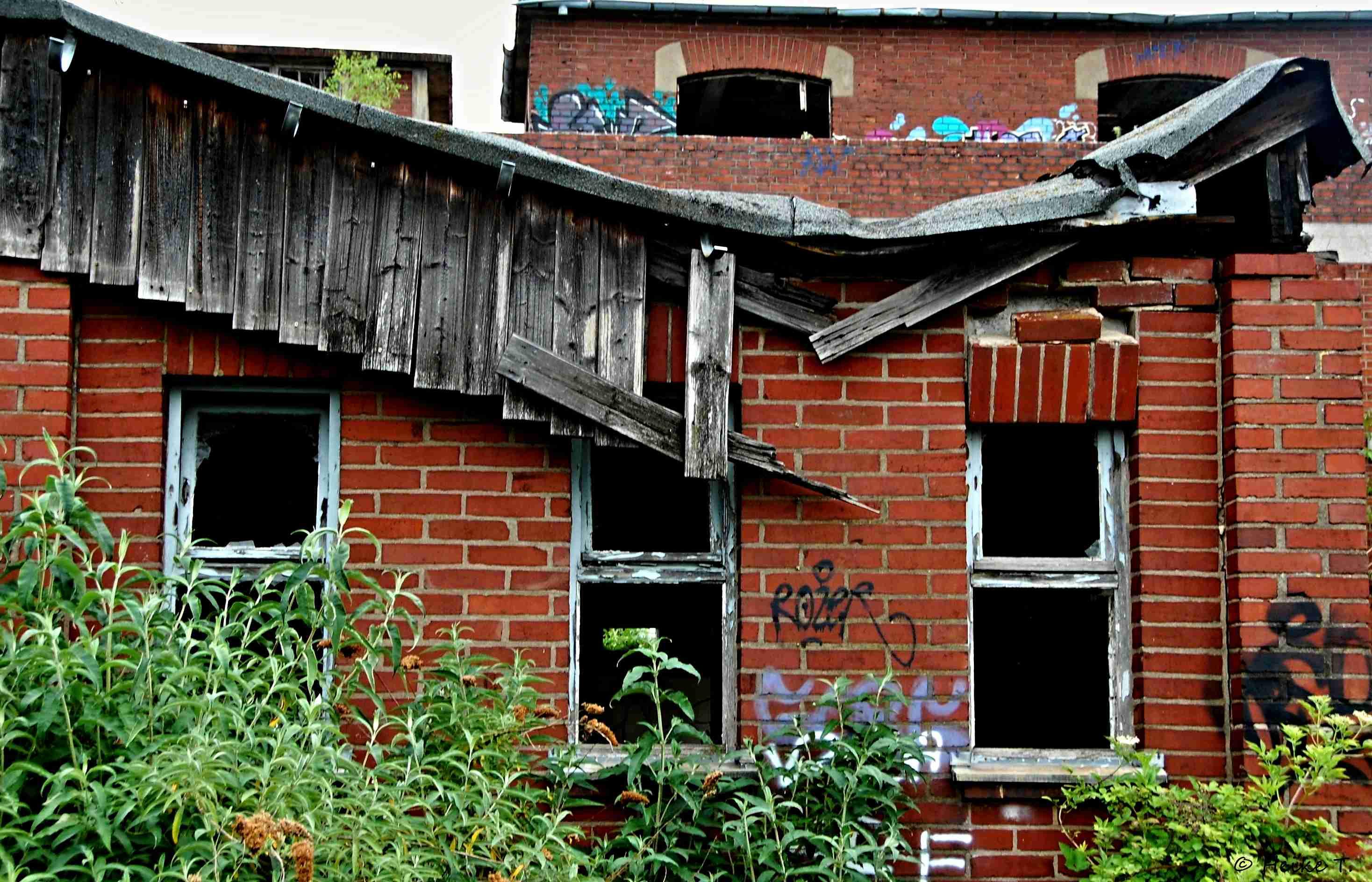 Eine Ruine aus roten Ziegeln mit beschädigtem Holzdach und zerbrochenen Fenstern. Pflanzen wachsen aus den Mauern. Graffiti ist an den Wänden zu sehen. Eine Ruine aus roten Ziegeln mit beschädigtem Holzdach und zerbrochenen Fenstern. Pflanzen wachsen aus den Mauern. Graffiti ist an den Wänden zu sehen.