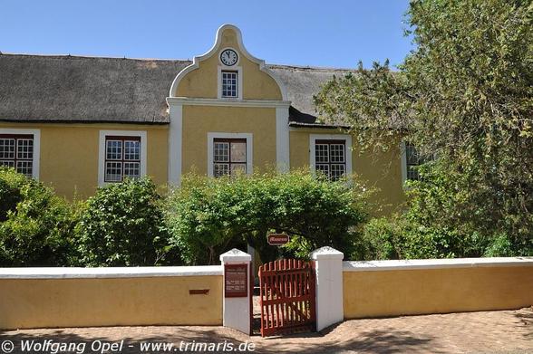 Das Foto zeigt ein Gebäude im holländischen Kolonialstil, das heute das Moravian Mission Museum und Archiv in Genadendal, Südafrika, beherbergt. 