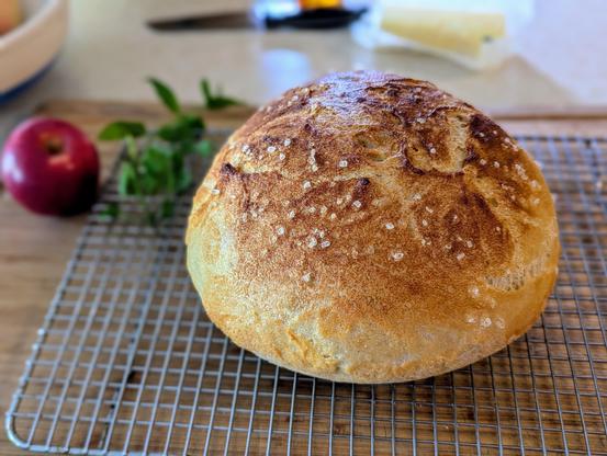 Photo of a freshly baked loaf of bread. It's sitting on a wire rack with an apple in the background.