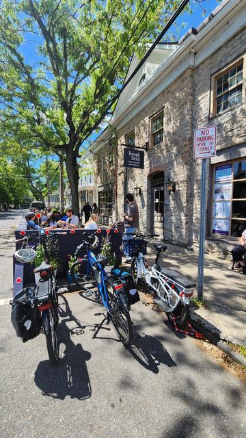Springtime scene: three ebikes parked at the edge of a parklet or "streatery" in front of a bookstore/cafe