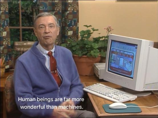 Screenshot of the Mister Roger's Neighborhood show. Mister Rogers sits in front of a mid-1990s-style PC, looking at the camera as he says, “Human beings are far more wonderful than machines.”