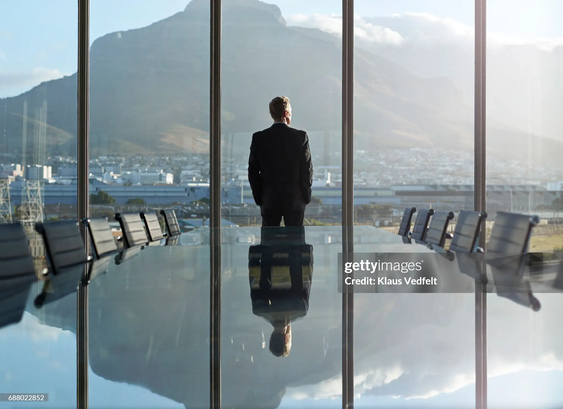 man standing infront of a glass window looking over at a mountain.