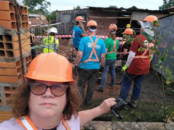 A woman takes a selfie with a group of house construction volunteers behind her.